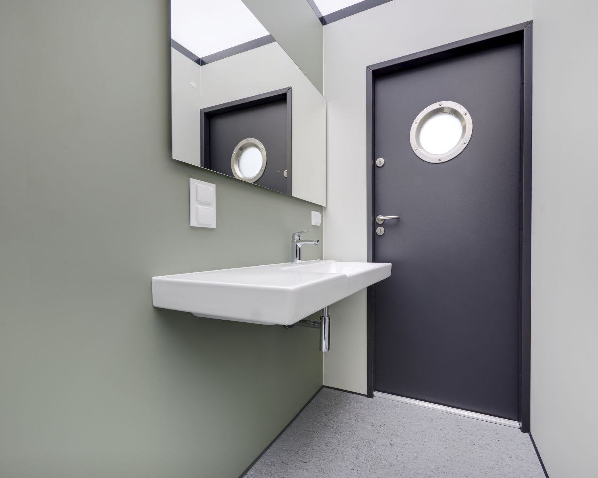 Wastafel en spiegel in badkamer met deur met rond raam.