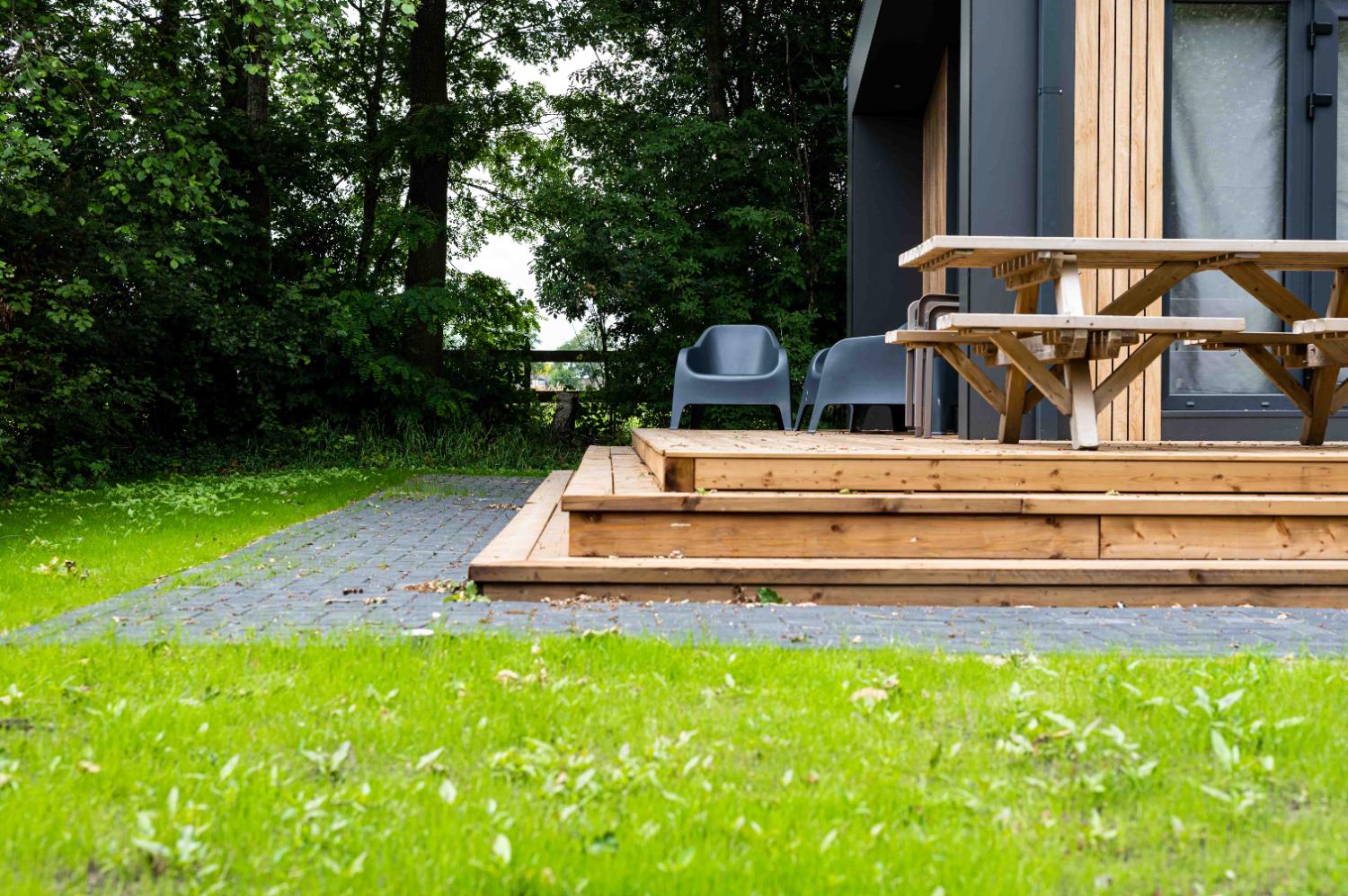 Lage hoek van een houten terras met meubels, gras en bomen.