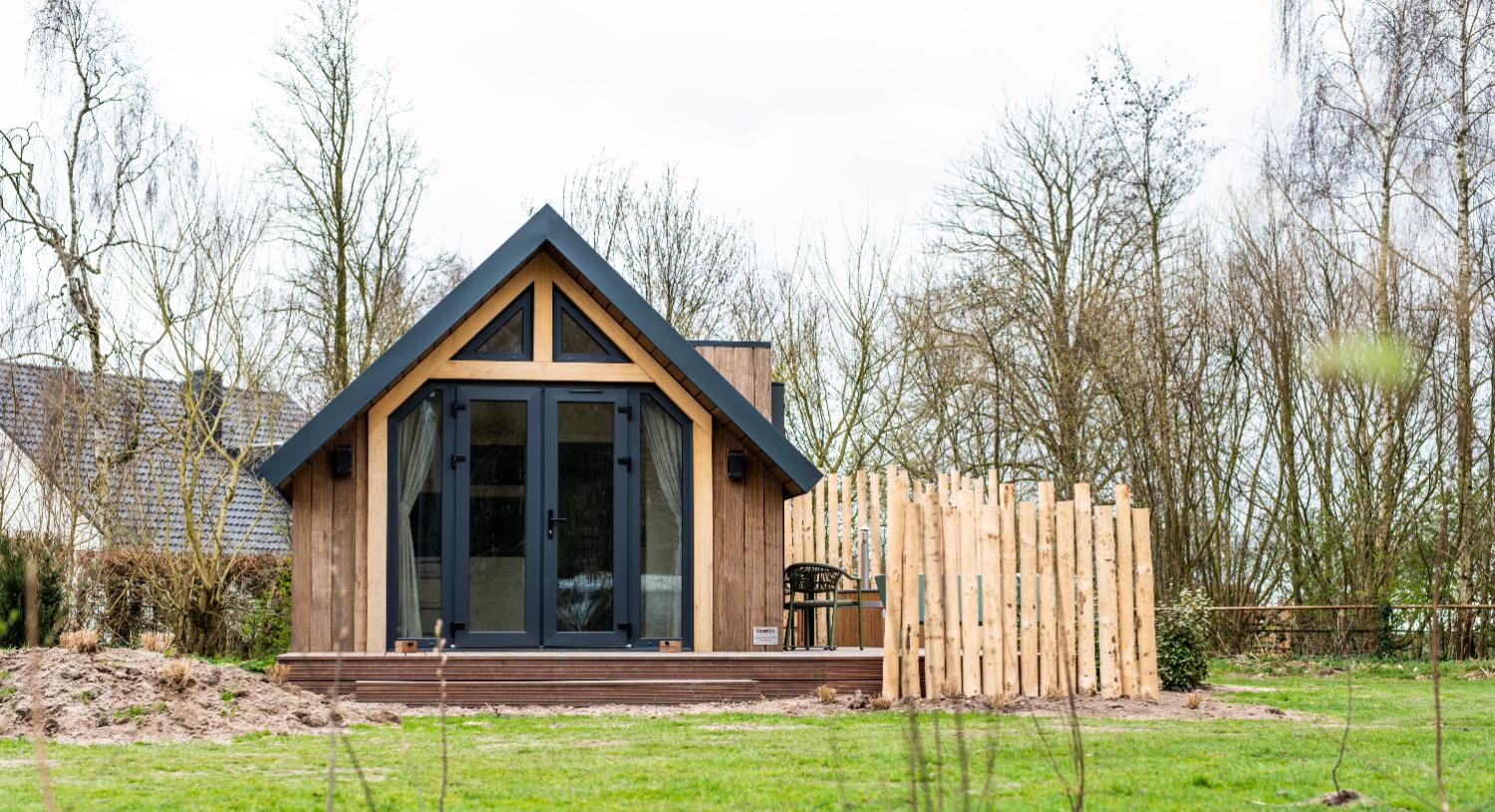 Kleine houten vakantiewoning met puntdak, terras en houten schutting.